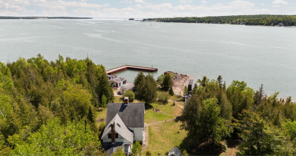 Aerial view overlooking South Pipe Island's lighthouse, lightkeeper's residence, private harbor, and wooded landscape in Michigan's Great Lakes.