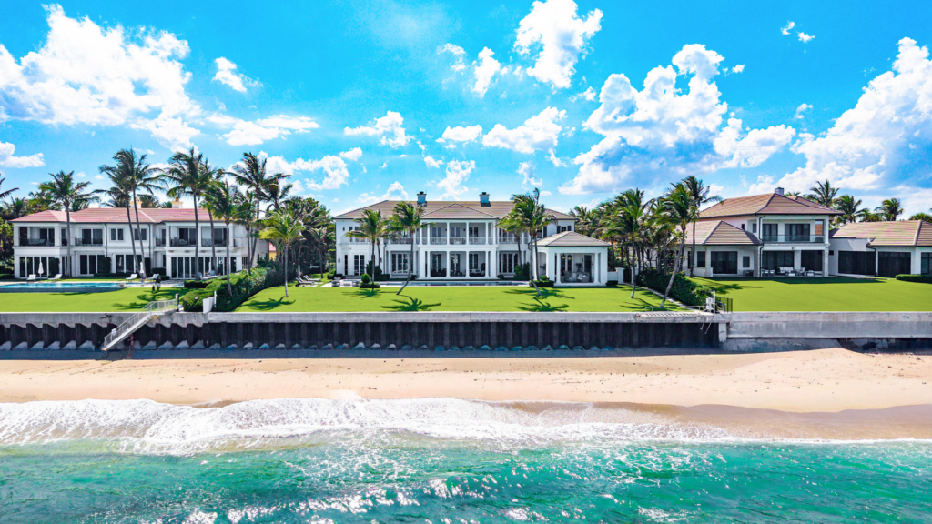 Oceanfront view of a luxury Manalapan estate with expansive lawn, palm trees and direct beach access.